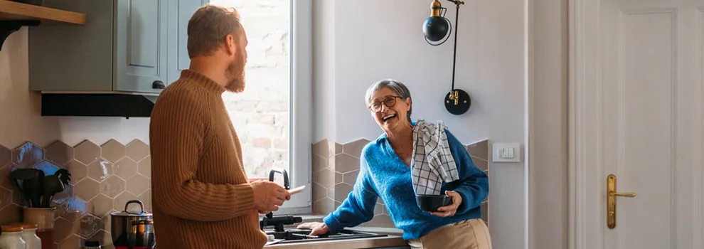 A man and woman are positioned in a cozy kitchen, smiling as they collaborate on meal preparation.