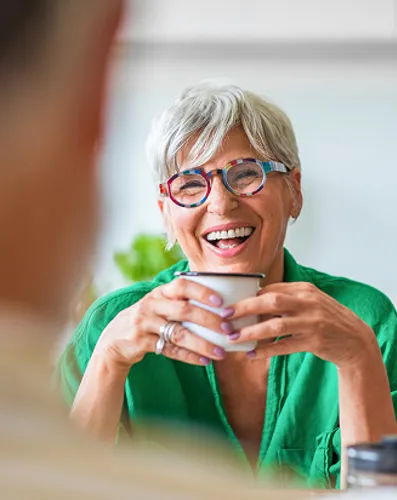 A woman wearing glasses and a green shirt smiles warmly at the camera.